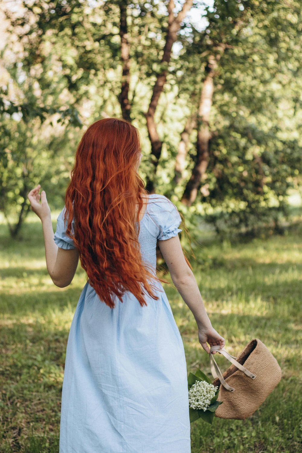 a woman with long red hair walking through a park
