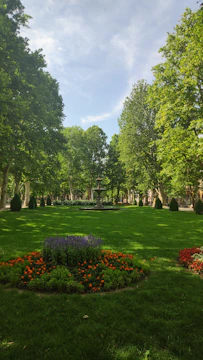 A lush green park with neatly laid carpet grass and vibrant flower beds under a clear sky.
