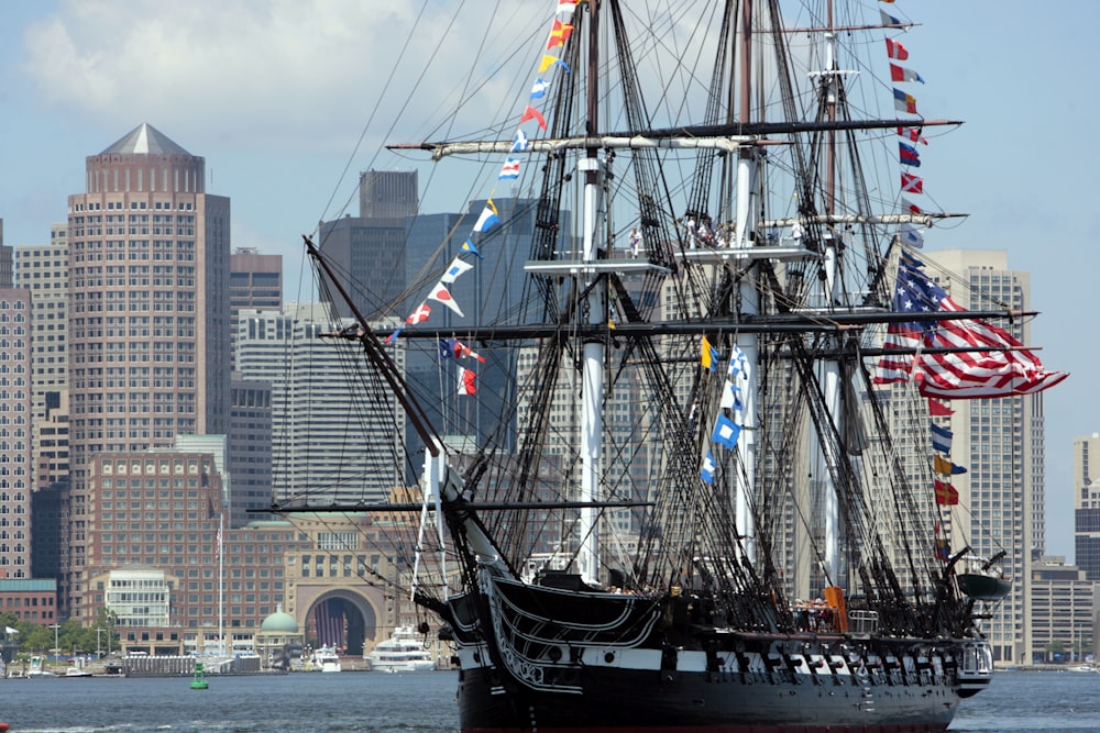 a large sailing ship in the water with a city in the background