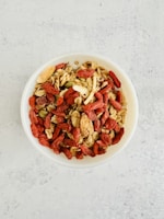 A colorful bowl of fresh mixed fruit with nuts and seeds.
