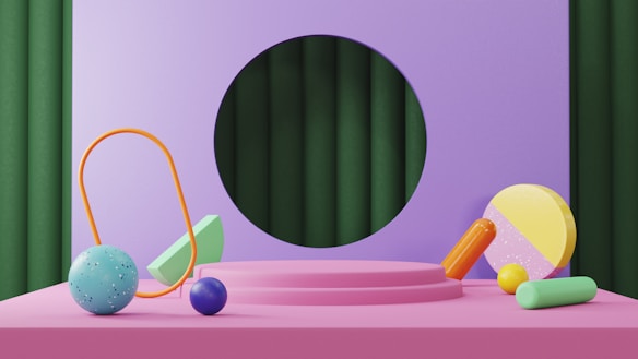 A vibrant, abstract scene featuring geometric shapes against a purple and green background. A pink platform hosts various objects, including a blue speckled sphere, a blue solid sphere, a yellow and pink semi-sphere, and an orange loop. A green rectangular prism and orange and green cylindrical shapes add to the composition.