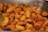 A close-up of roasted sweet potato wedges, seasoned with herbs and spices, arranged haphazardly in a metal tray. The potatoes are crispy and slightly charred on the edges, adding to their appetizing presentation.