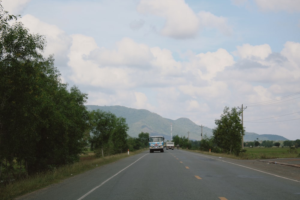 a truck driving down a road next to a lush green forest