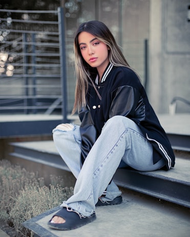 An outdoor shot of a person sitting on concrete steps, wearing layered fnr apparel pieces with a relaxed, urban vibe.