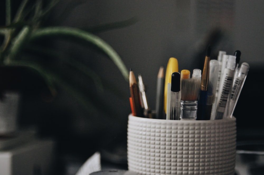 a cup filled with pens and pencils on top of a desk