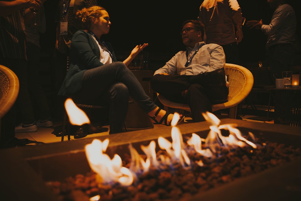 a man and woman sitting next to a fire pit