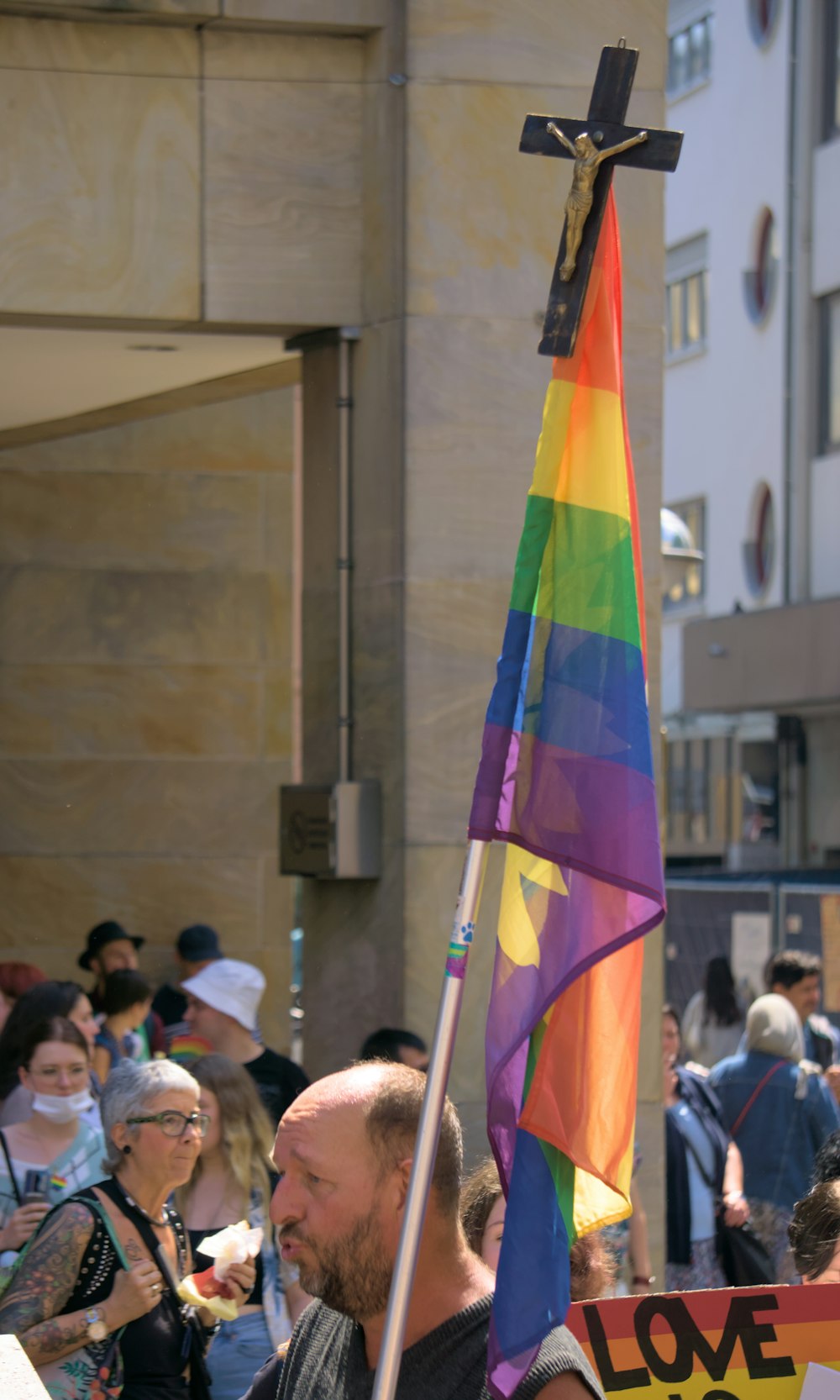 a man holding a cross and a rainbow flag