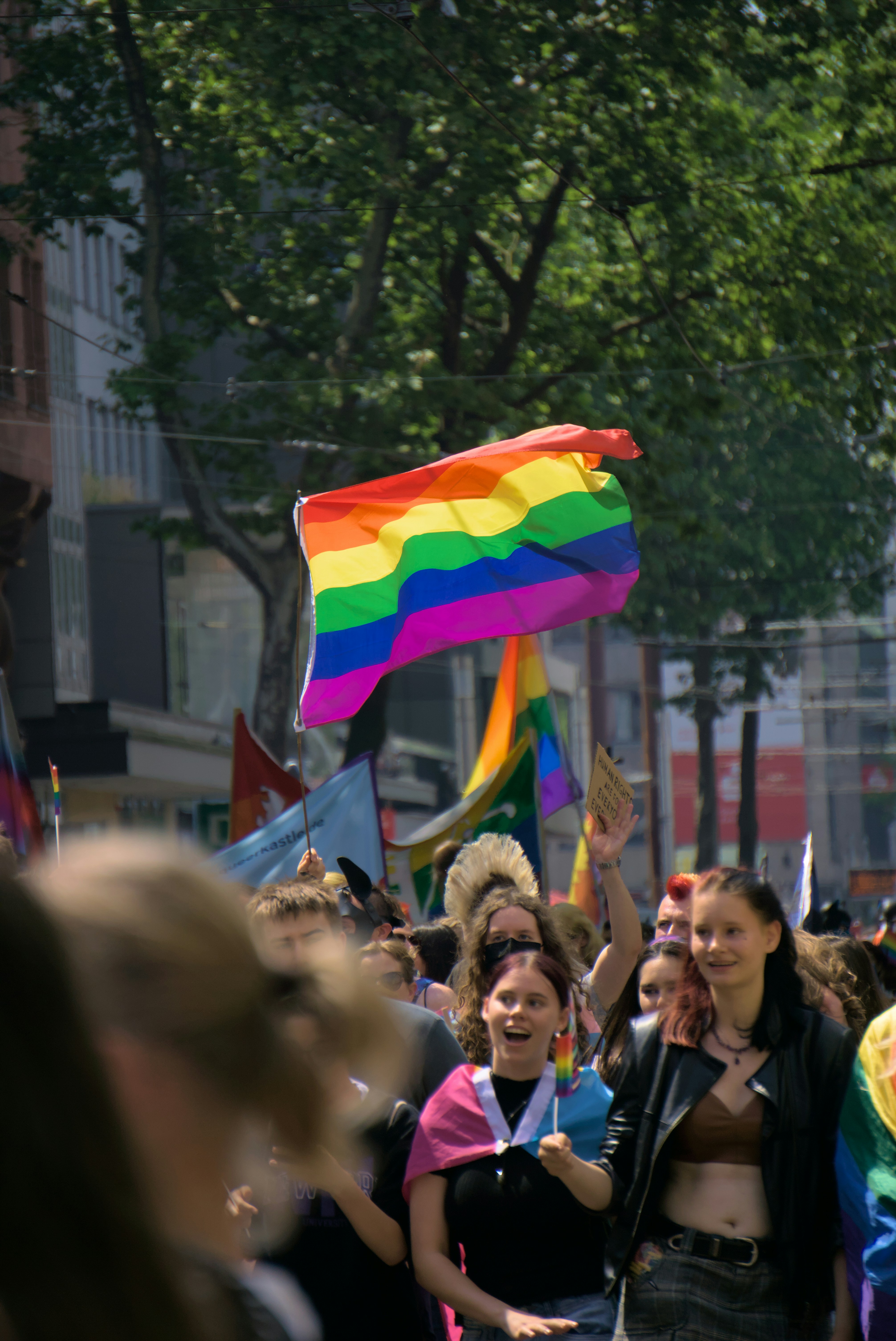 Un grupo de personas caminando por una calle con una bandera del arco iris
