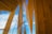 Wooden architectural beams and panels stretch upwards towards a bright blue sky with scattered clouds. Transparent glass elements intersect with the wooden structure, adding a modern touch.