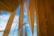 Wooden architectural beams and panels stretch upwards towards a bright blue sky with scattered clouds. Transparent glass elements intersect with the wooden structure, adding a modern touch.