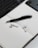 A black pen with 'envato' printed on it rests on an open lined notebook. Two wireless earbuds are placed nearby on the notebook. The corner of a laptop keyboard and a smartphone are partially visible, creating a workspace setting.