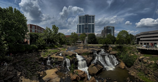 a waterfall in the middle of a river with a city in the background