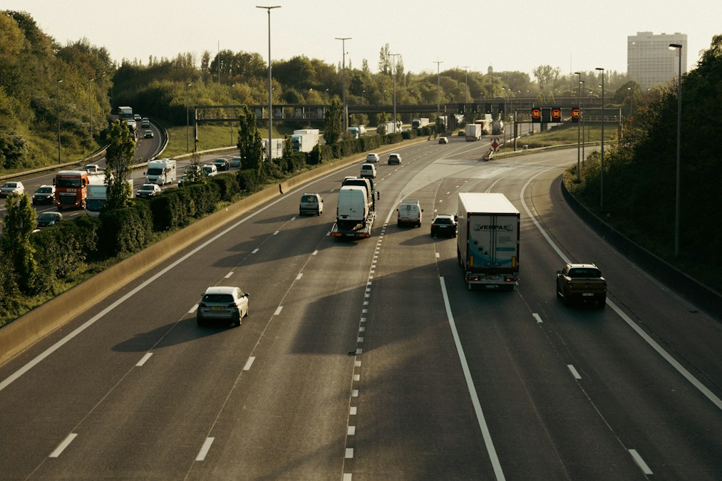 Une autoroute à plusieurs voies avec voitures et camions, bordée d'arbres et surmontée de panneaux de signalisation