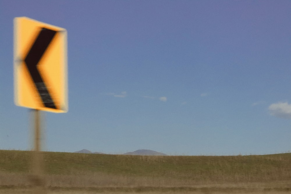 a yellow and black arrow sign in the middle of a field