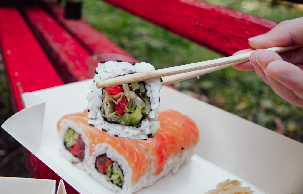 a person holding a chopstick over a sushi roll