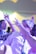 A group of people are dancing energetically at a social event. The scene is lively with bright, colorful lighting casting hues of purples and yellows across the room. The individuals are dressed formally, with one person wearing a white shirt and a tie, and others around them seem to be in motion with raised arms and blurred movements.