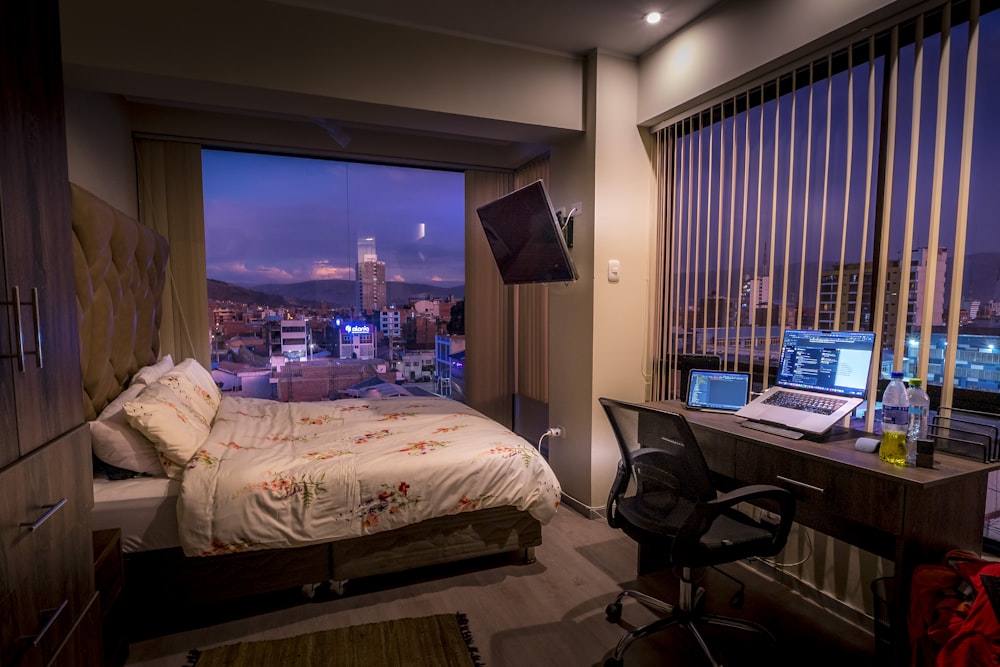 a bedroom with a bed, desk, and laptop computer