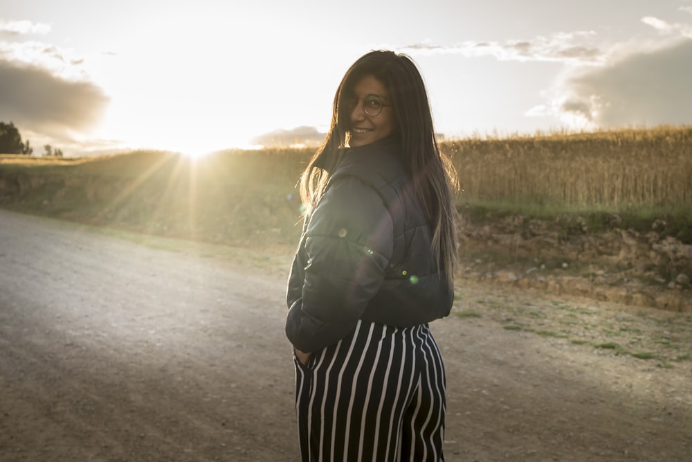 a woman standing in the middle of a dirt road