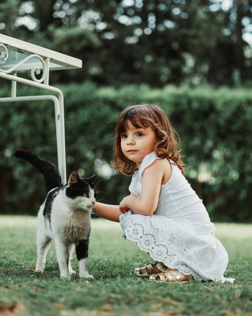 a little girl kneeling down next to a black and white cat