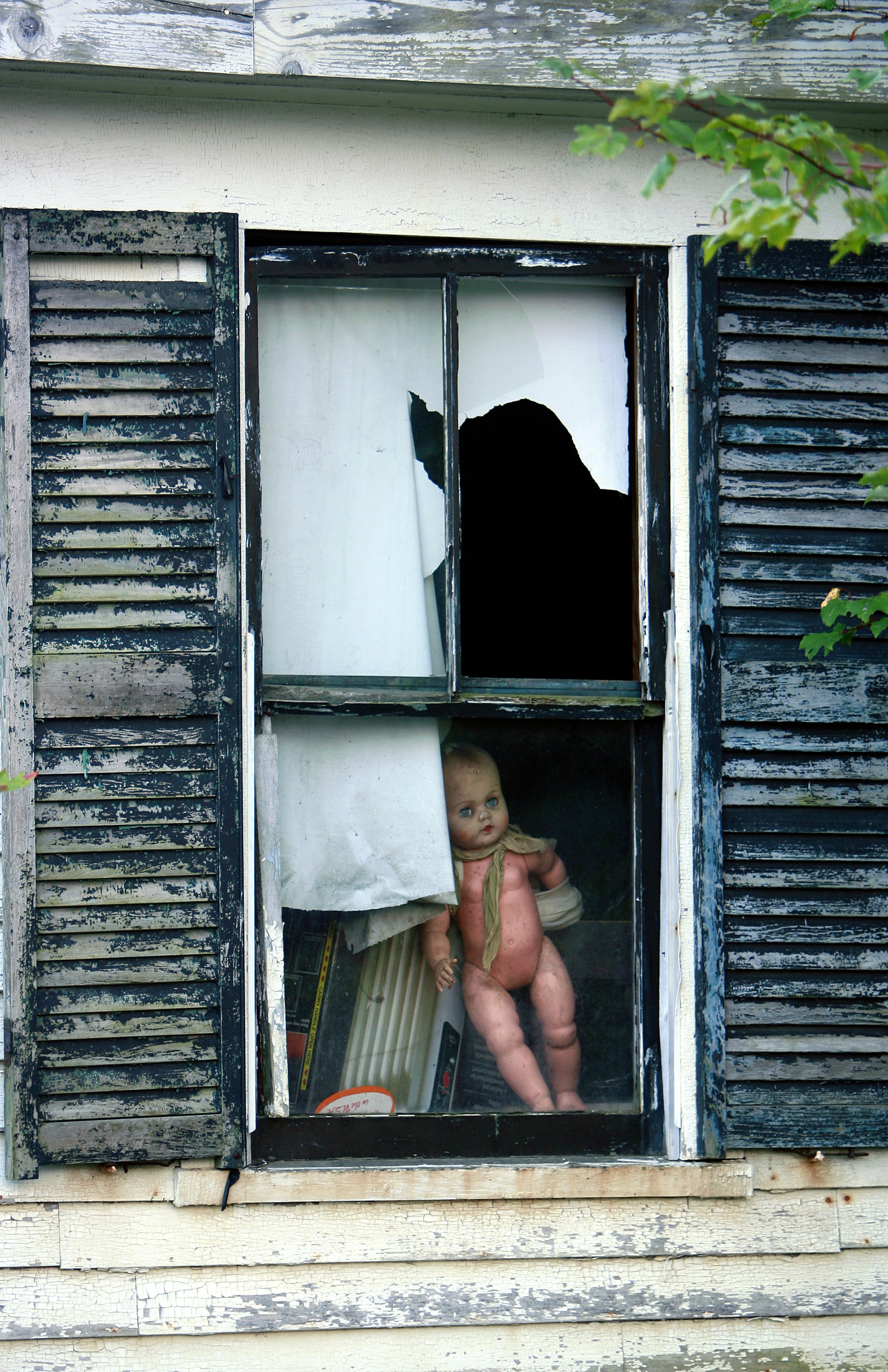 a baby doll sitting in a window of an old house