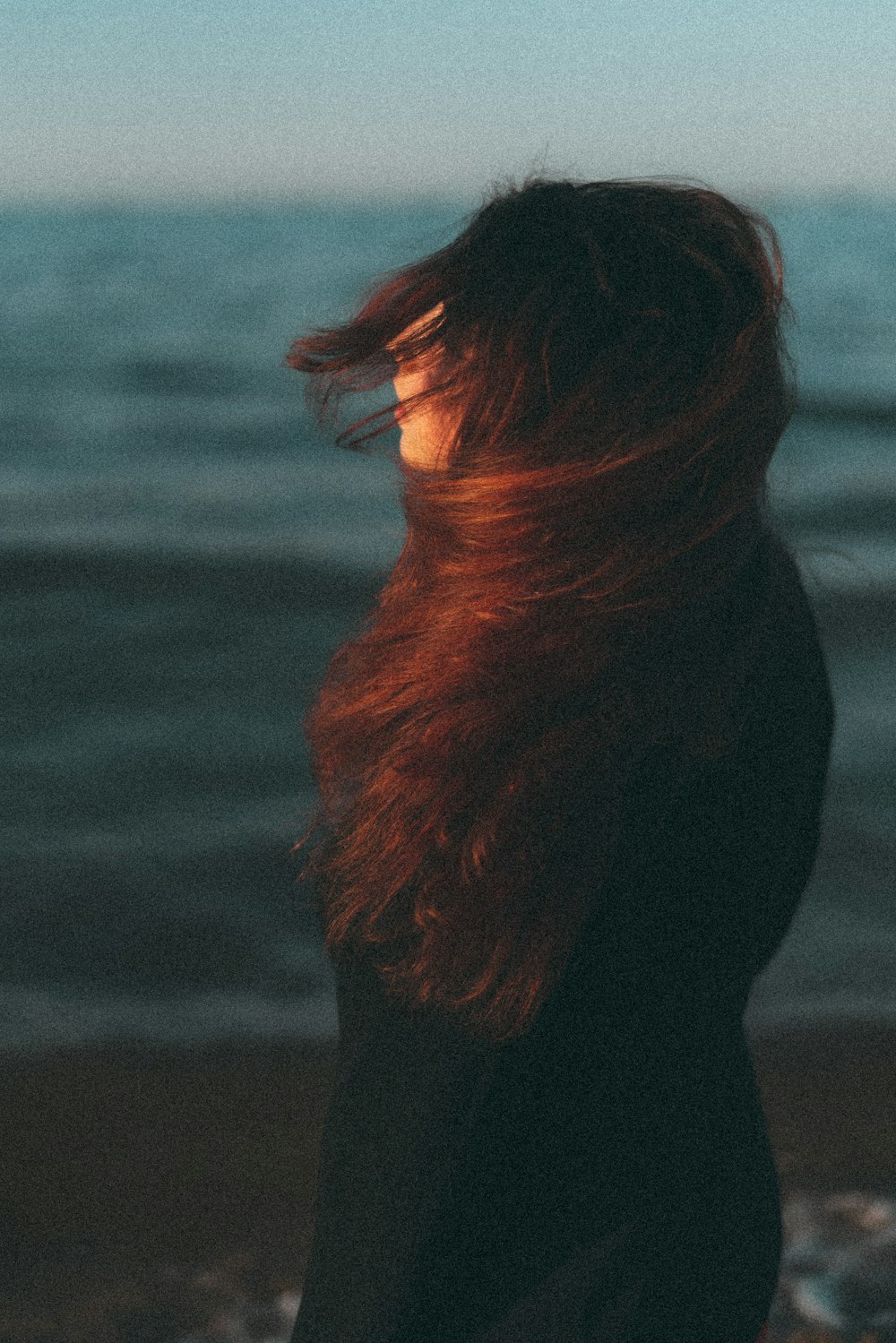 a woman standing on a beach with her hair blowing in the wind