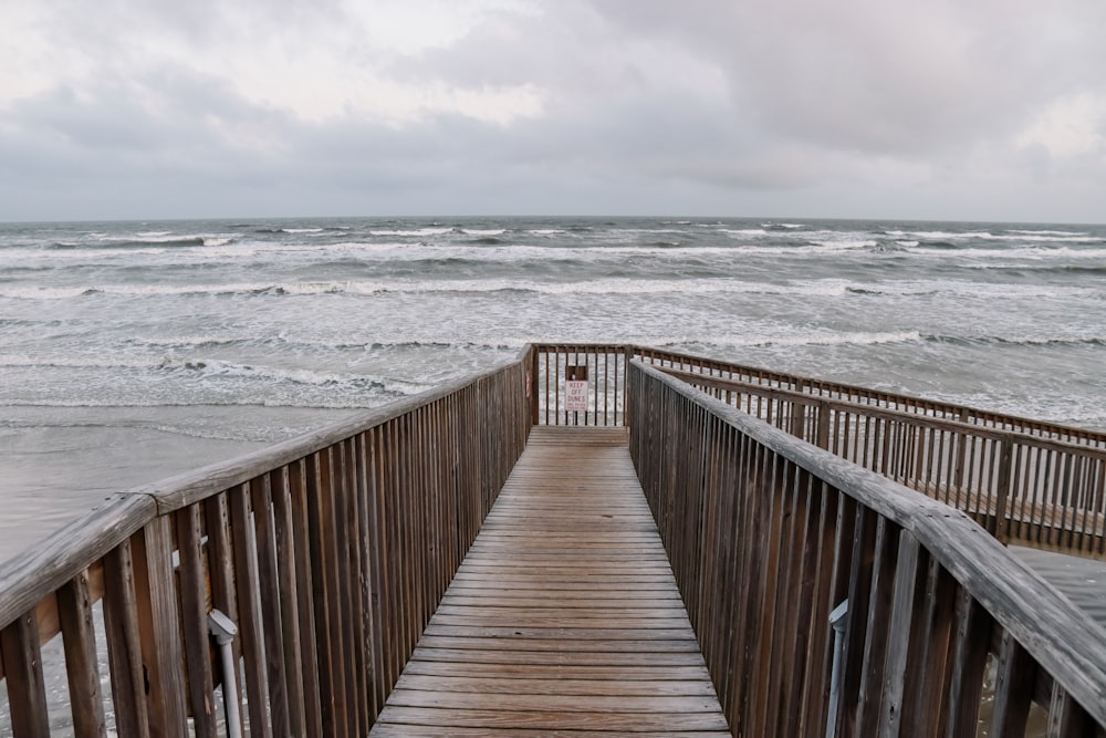 a wooden walkway leading to the ocean on a cloudy day