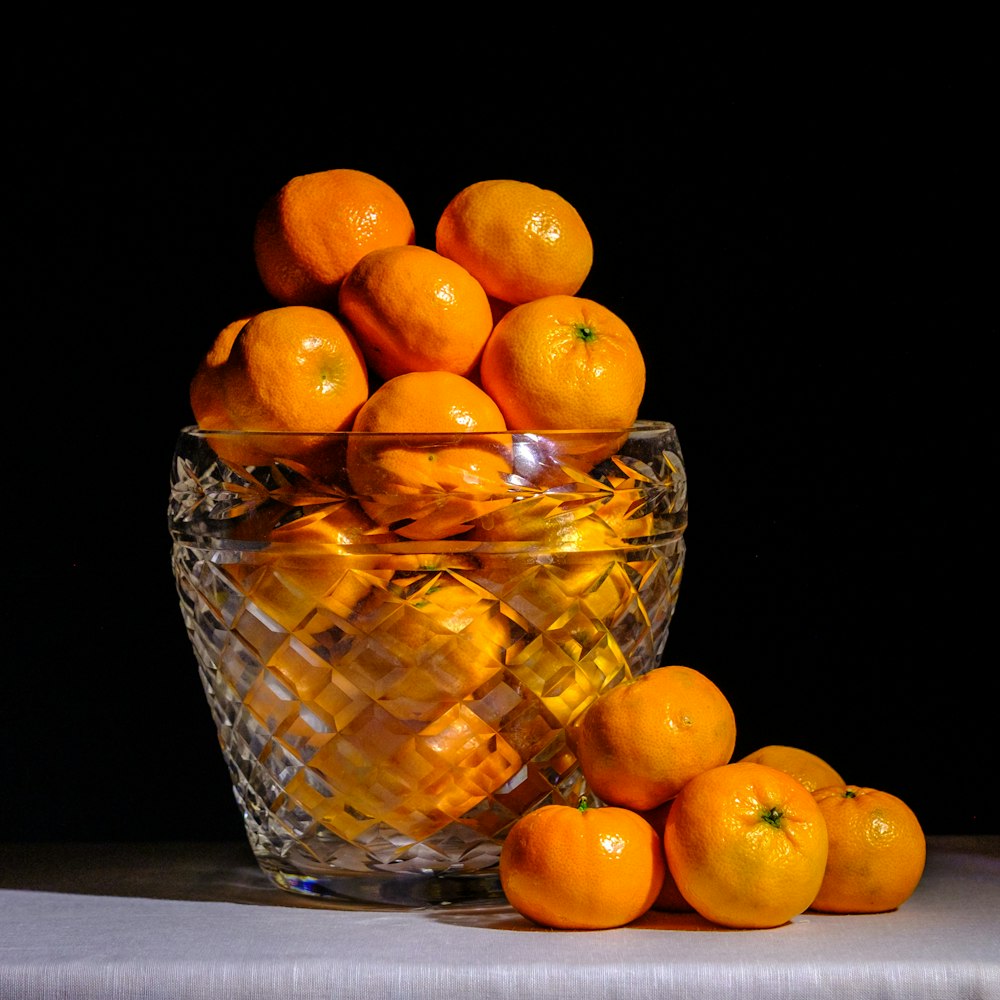 a glass bowl filled with oranges on top of a table