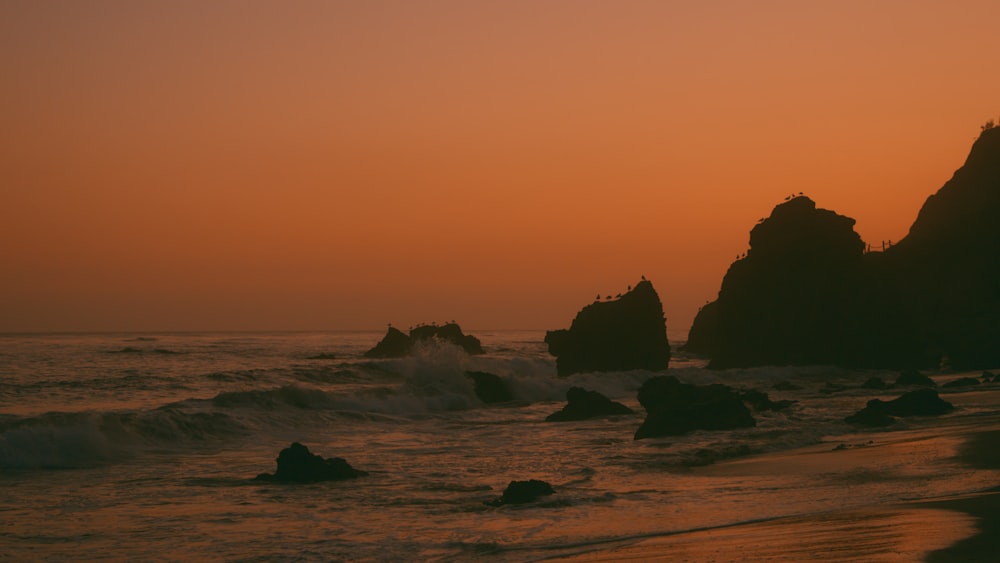 the sun is setting over the ocean with rocks in the foreground