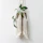 Close-up of a stylish macramé plant hanger holding a trailing fern against a soft green wall.