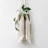 A macrame plant hanger holds a woven basket with trailing green vines. The hanger is made of white cords that form a decorative pattern with long fringes. The plant features broad green leaves with light green variegation.