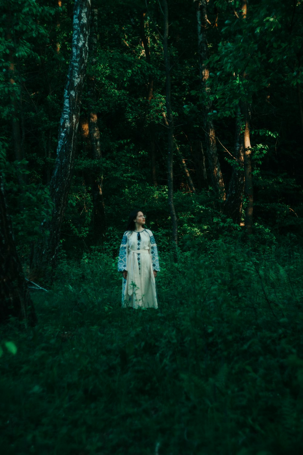 a woman in a white dress standing in a forest