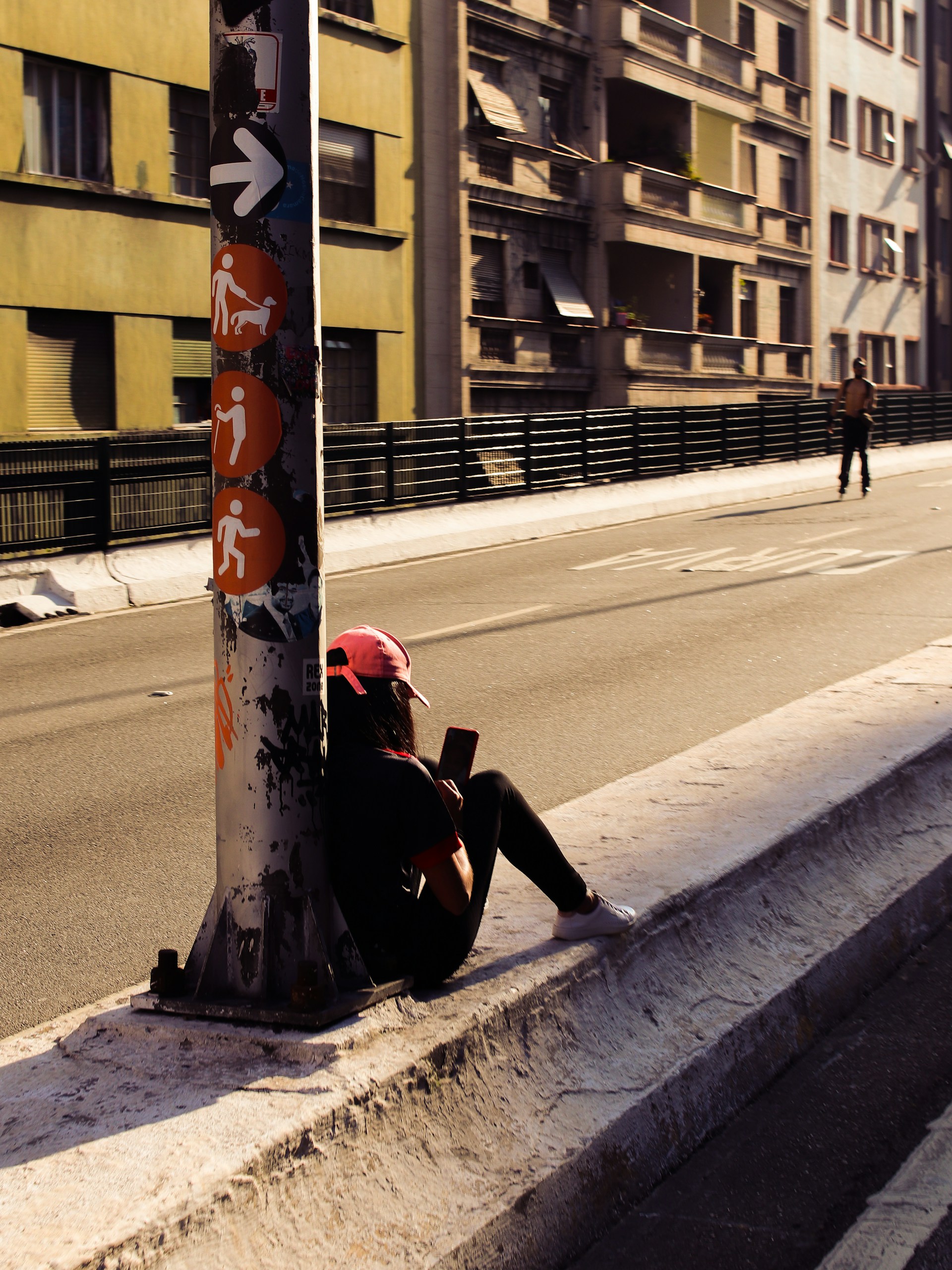 a person sitting on the side of a road next to a pole