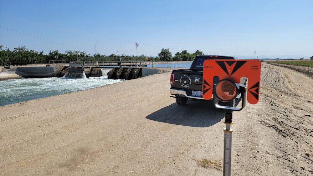 a truck driving down a dirt road next to a body of water