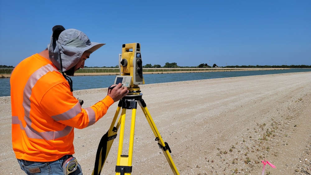 a man in an orange jacket is looking at a map on a tripod