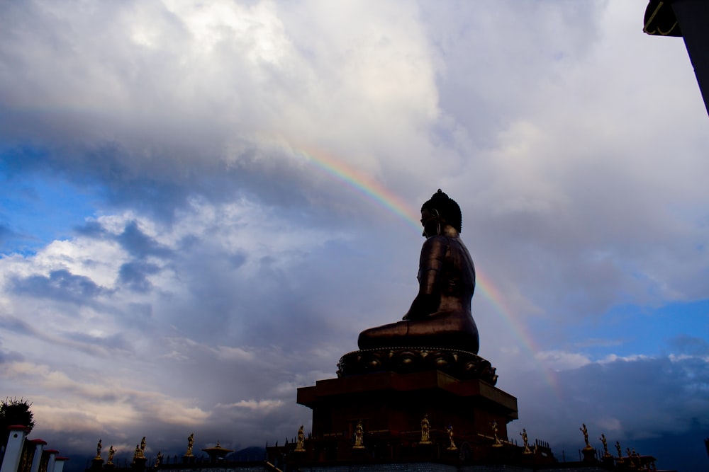 a buddha statue with a rainbow in the background