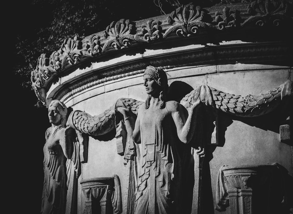 a black and white photo of statues on a building