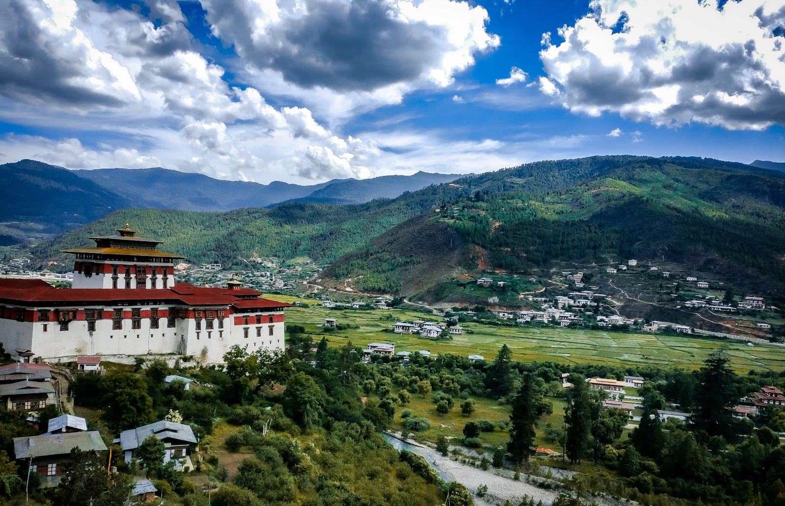 Rinpung Dzong seen from the hillside path above, the Paro valley's green fields and villages spread beyond