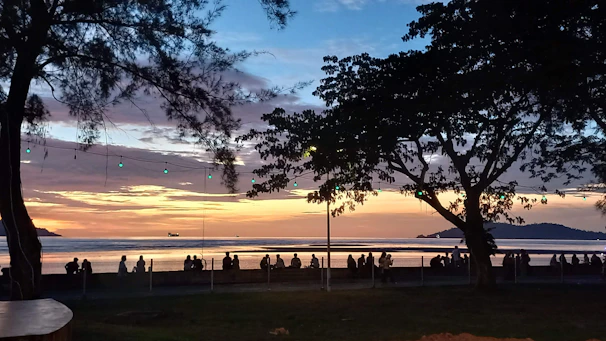 Sunset view of a lively beach crowd dancing near the ocean with colorful festival lights.