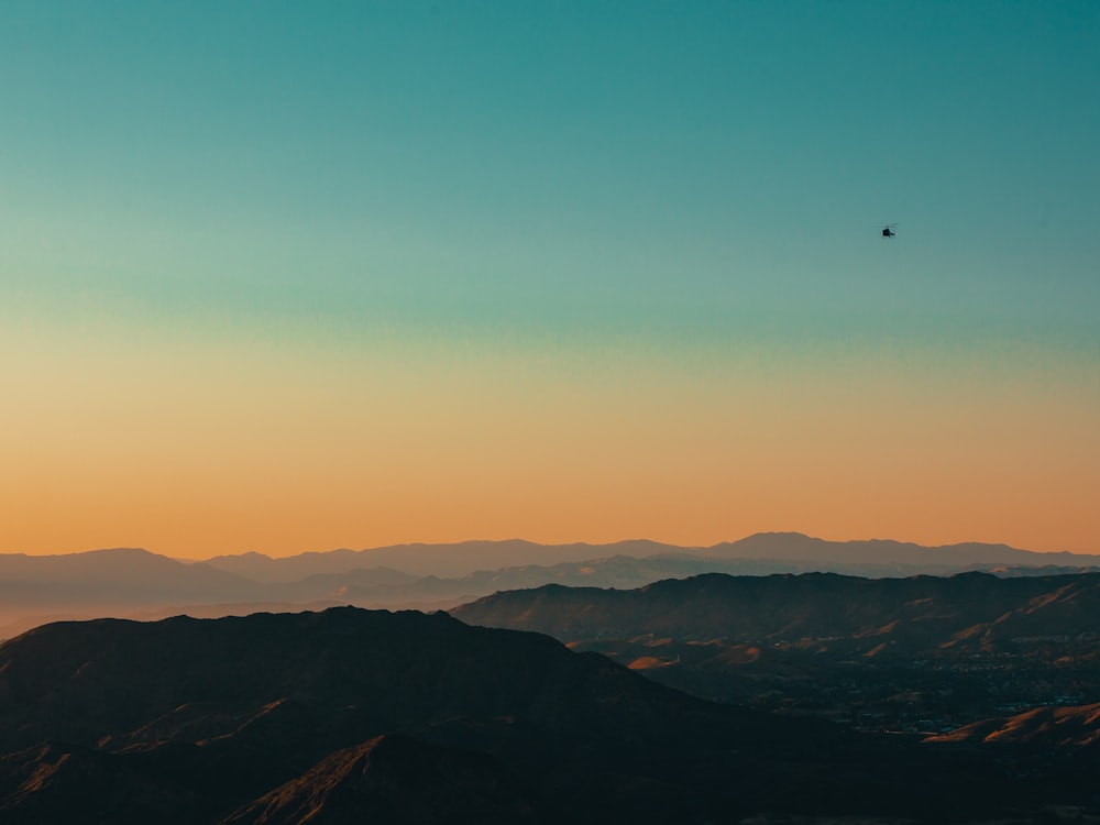 a bird flying over a mountain range at sunset