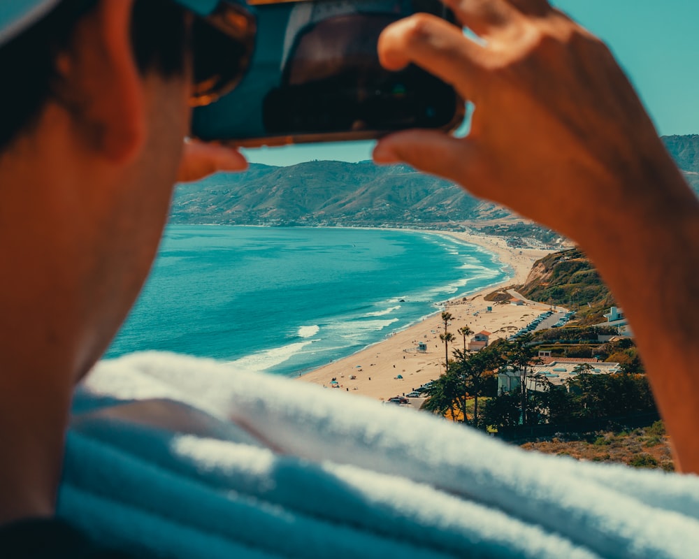 a man taking a picture of a beach with his cell phone