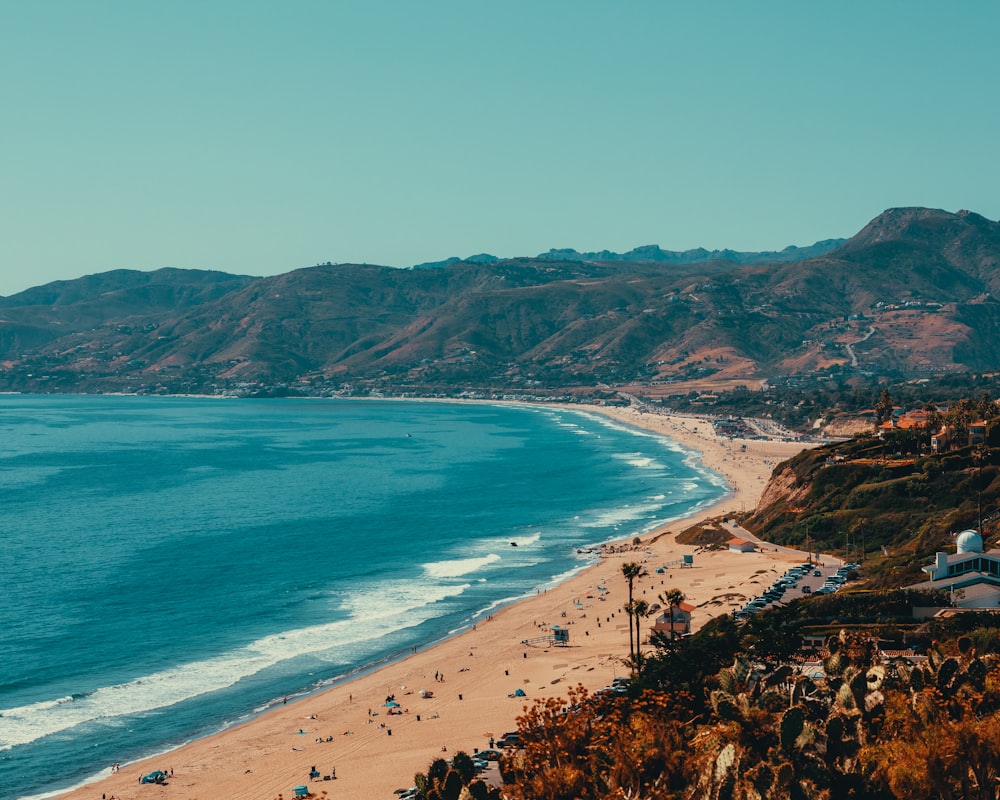 a beach with a lot of people and mountains in the background