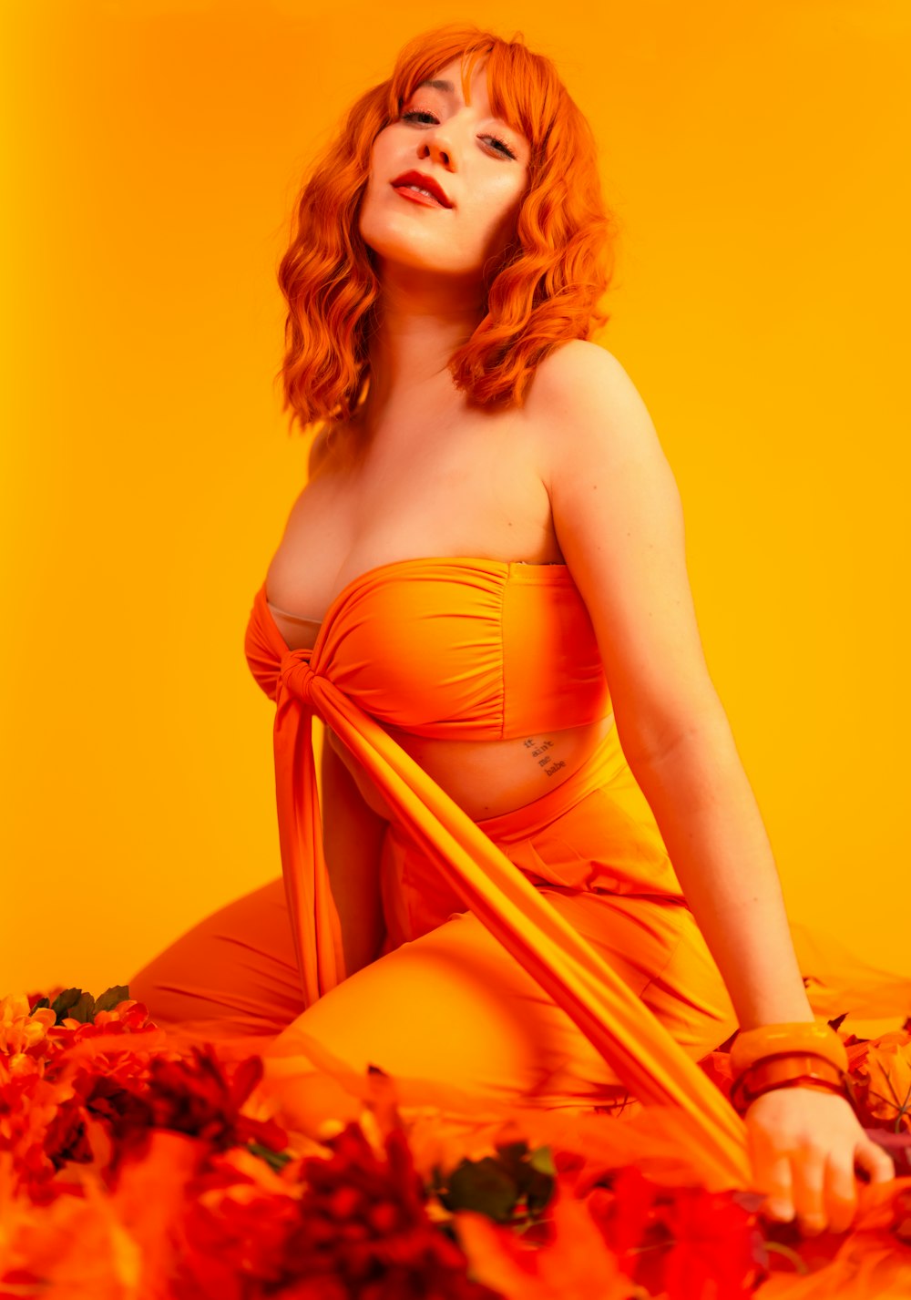 a woman in an orange dress sitting on a bed of flowers