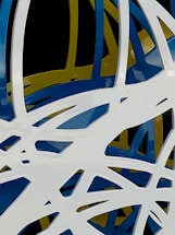 An abstract composition featuring intertwined and overlapping organic shapes in white, blue, and yellow against a black background. The shapes are sleek and glossy, creating a dynamic and modern aesthetic.
