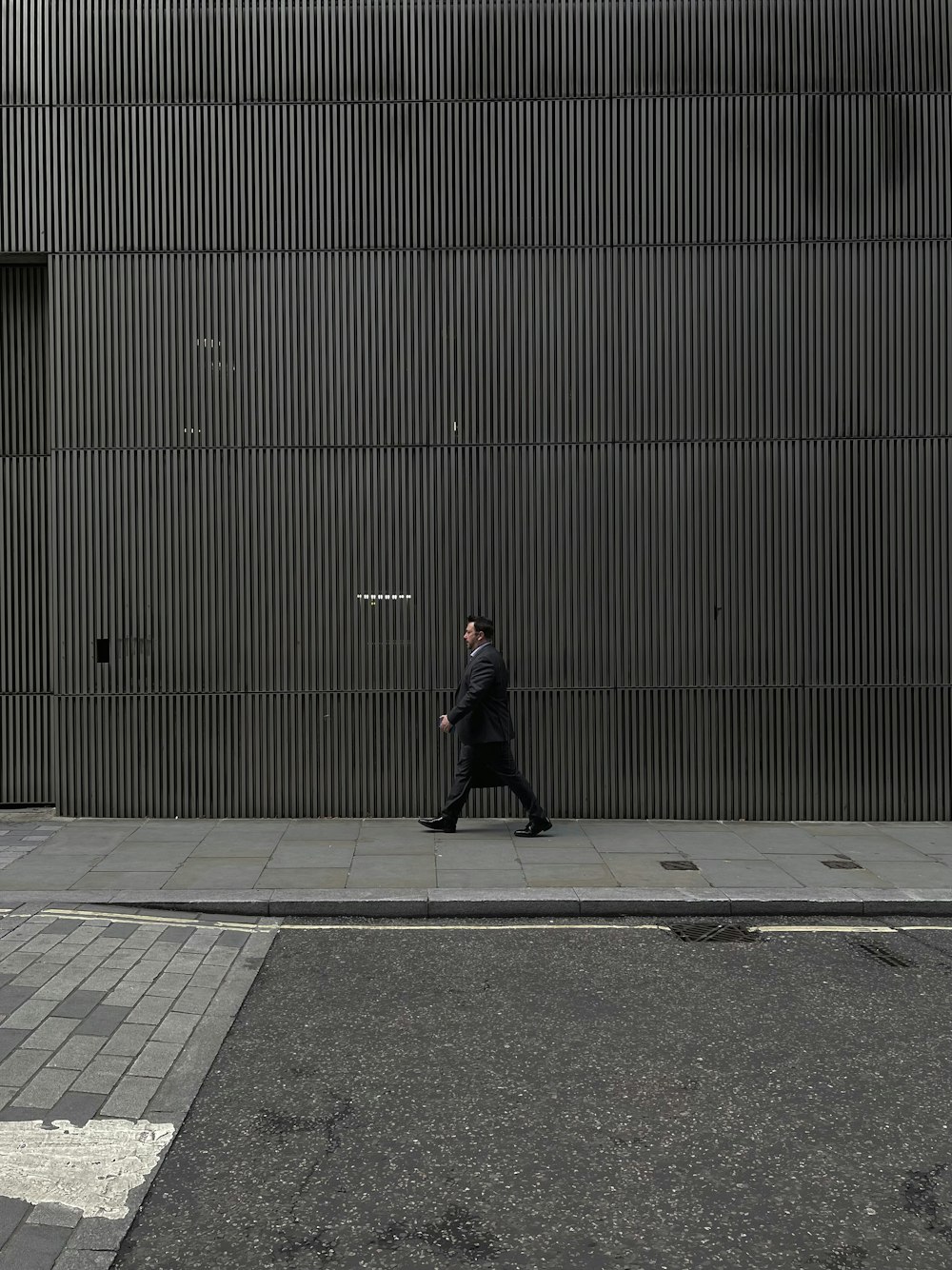 a man walking down a sidewalk next to a tall building