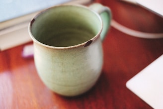 A close-up of a smooth, hand-glazed ceramic mug with subtle earth tones resting on a wooden table.