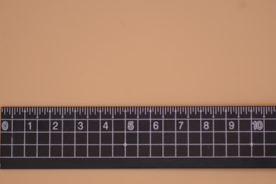 A black ruler with white markings is placed on a flat light-colored surface. It features a grid pattern with both numerical and fractional increments.