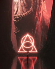 A person stands facing a large, illuminated geometric shape in a dark, cavernous space. The shape is a glowing triangular symbol composed of interlocking circles, emitting a vibrant red light that casts reflections on the polished floor. The surrounding walls appear rugged and monumental, enhancing the surreal and mysterious atmosphere.