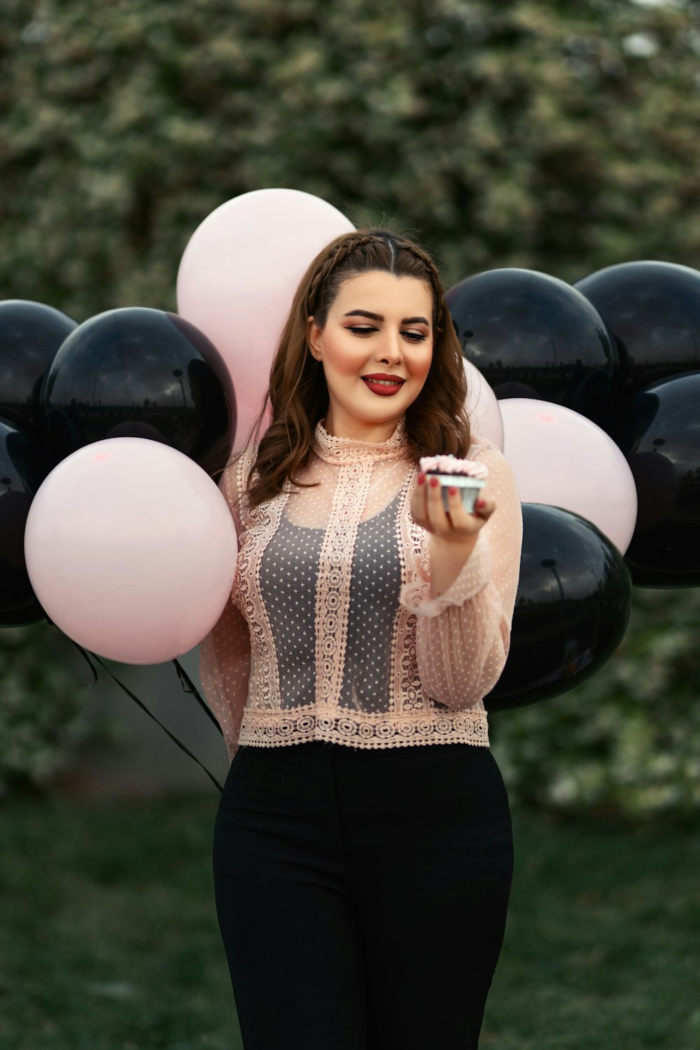 a woman holding a cupcake in front of a bunch of balloons