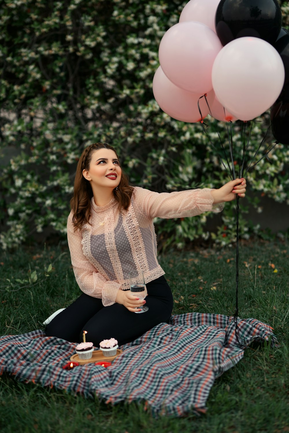 a woman sitting on a blanket holding a bunch of balloons