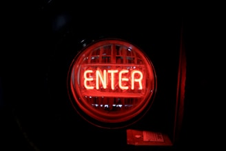 A round neon sign displaying the word 'Enter' in bright red letters, set against a dark background.